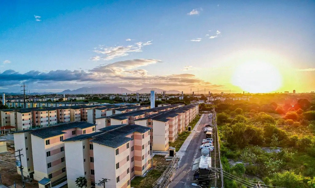 Prédios das unidades habitacionais do Programa Minha Casa, Minha Vida vistos de cima, com pôr do sol ao fundo.